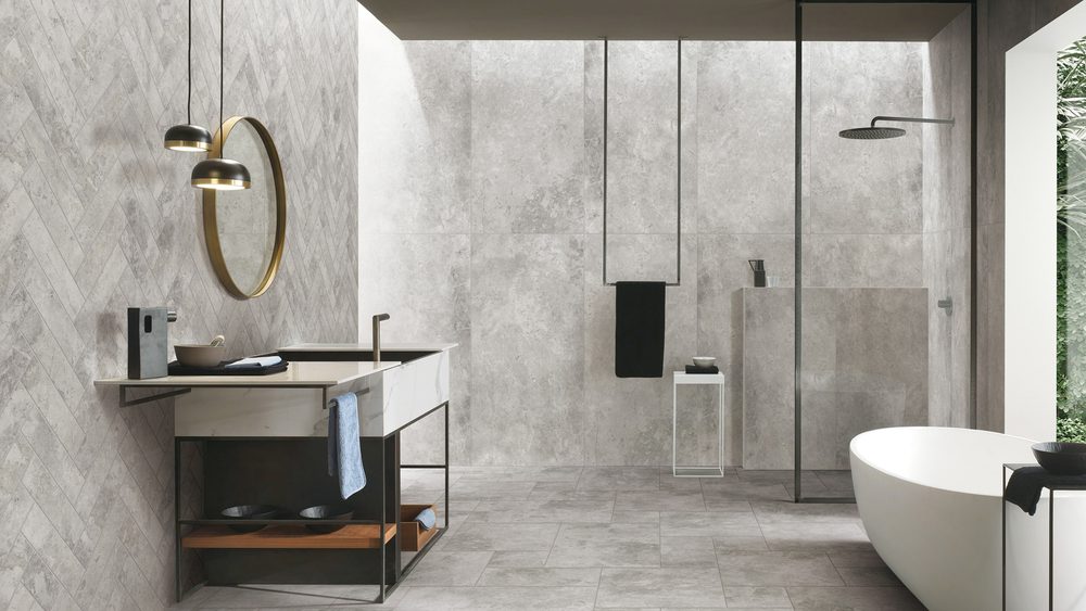 Stoneworld Tundra grey limestone-look porcelain tiles on the walls and floor of a bathroom with a freestanding bath