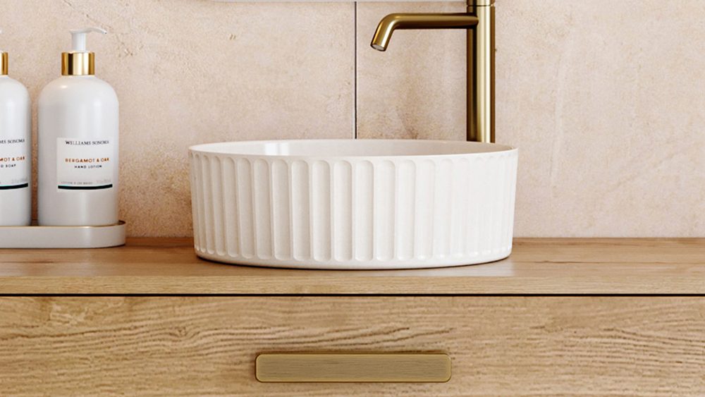 A fluted Timberline Allure basin in white on a timber wall hung vanity with brushed brass tapware