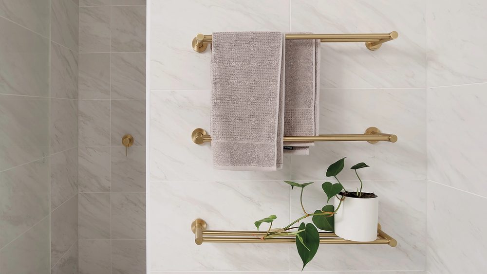 Phoenix Radii towel rails and shelf in brushed gold on a tiled bathroom wall