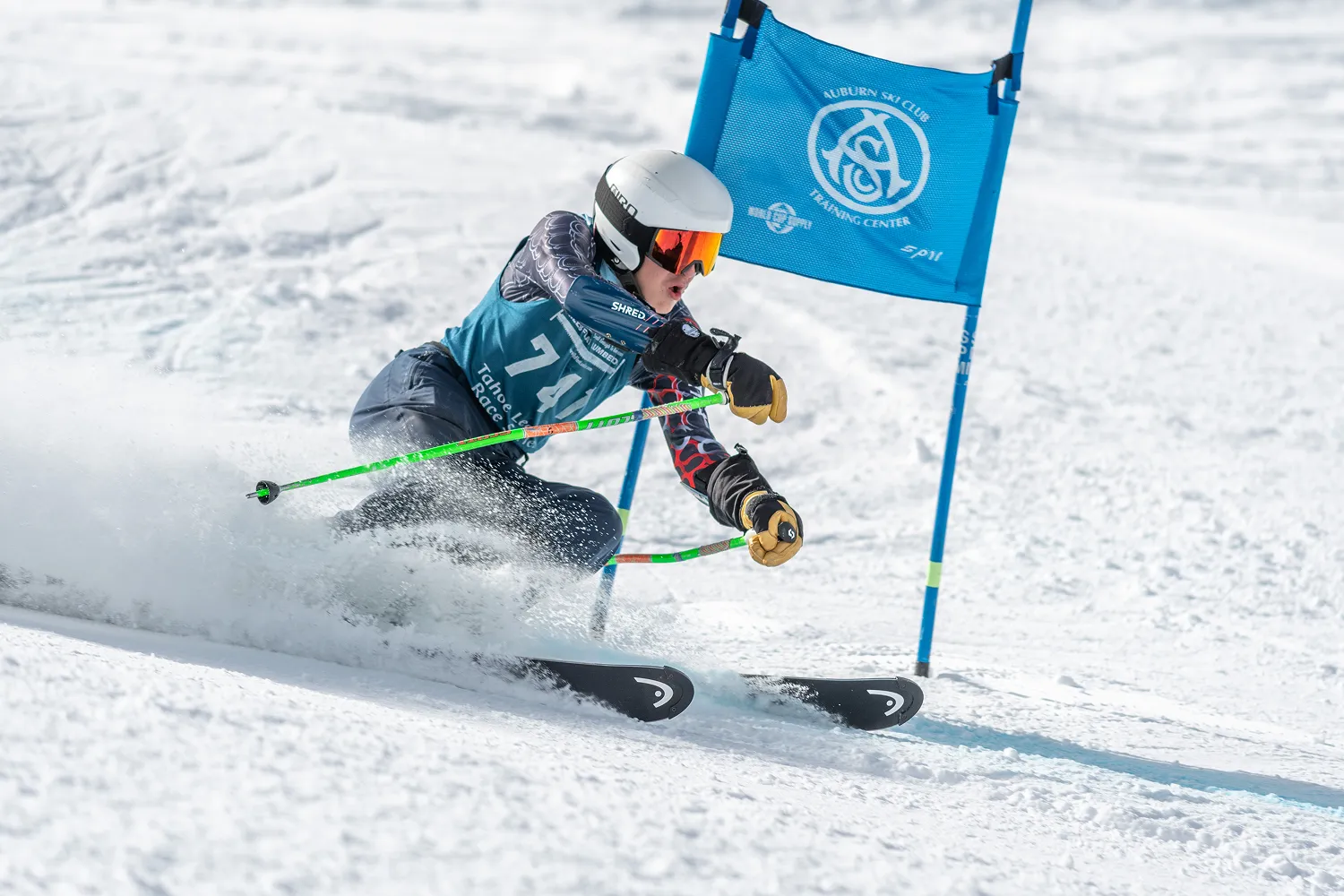Skier racing down snowy slope turning sharply around a blue gate marked Auburn Ski Club.