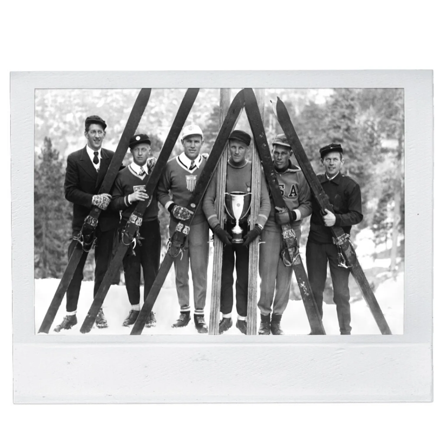 Six men standing in a row with vintage skis, one holds a trophy, dressed in early 20th-century attire.
