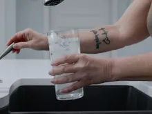 Hand filling a drinking glass with clear water from a kitchen sink faucet.