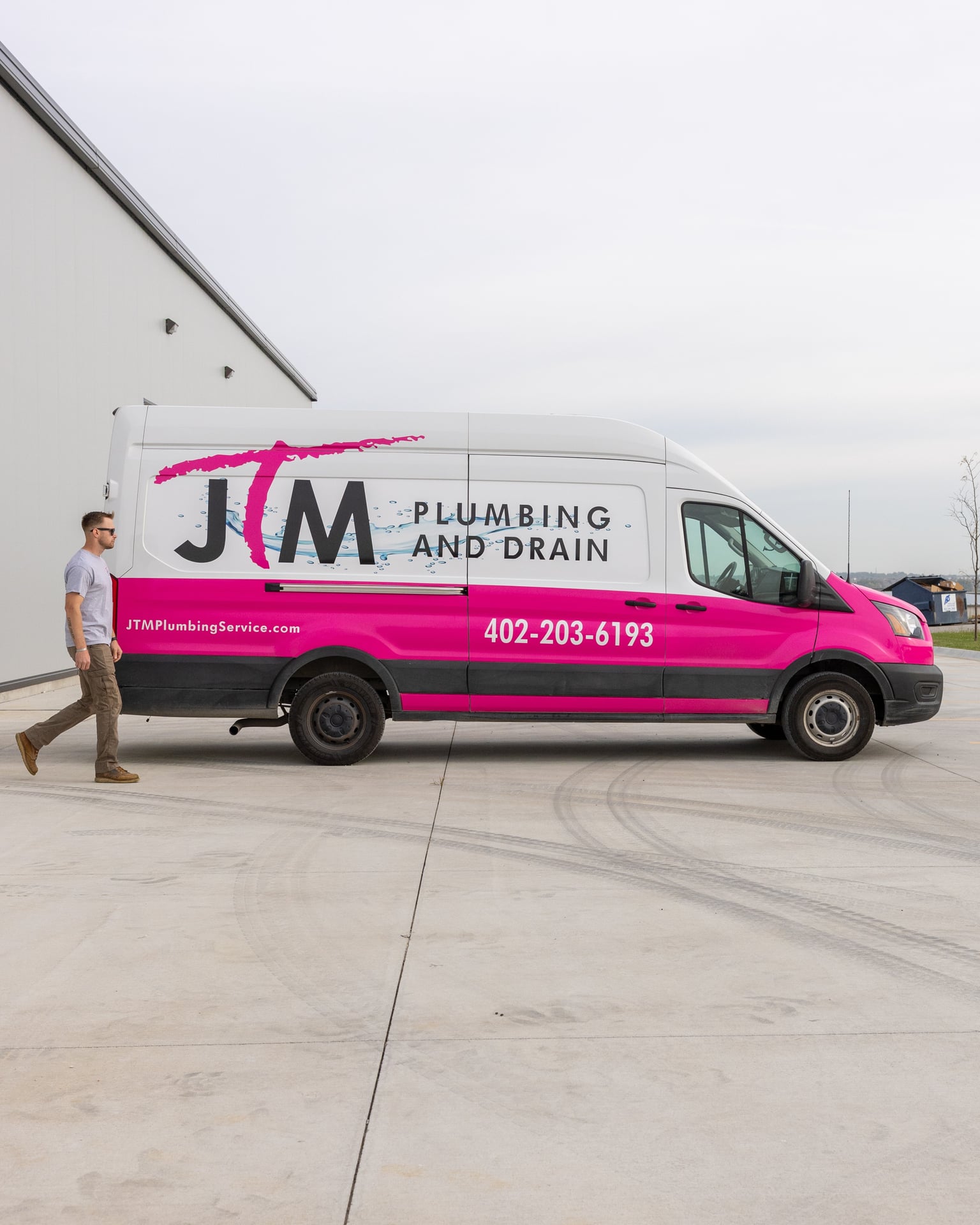 JTM Plumbing & Drain technician walking beside the company van outside a light industrial building.
