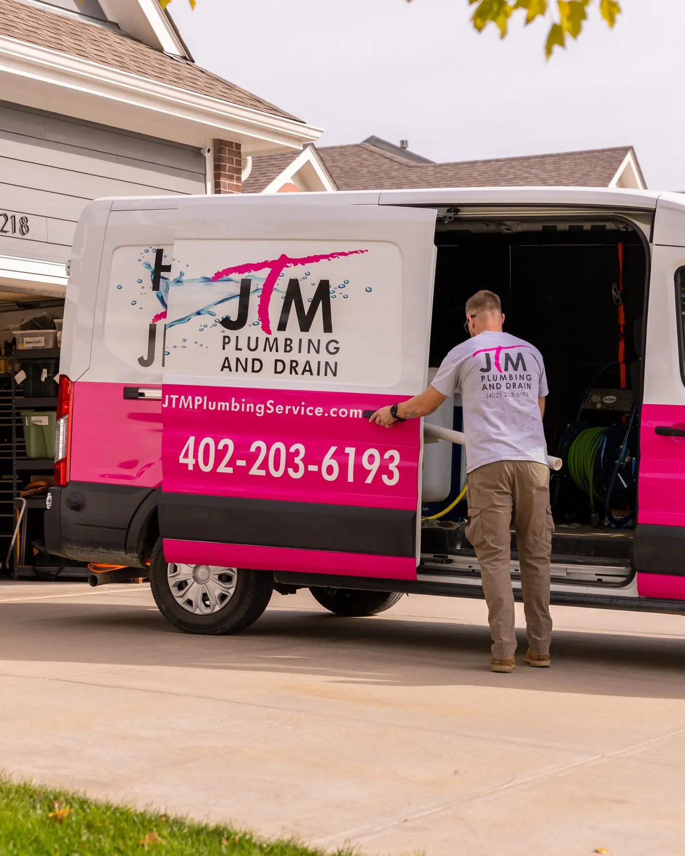 JTM Plumbing & Drain service van parked in a driveway as a technician retrieves equipment from the back doors.
