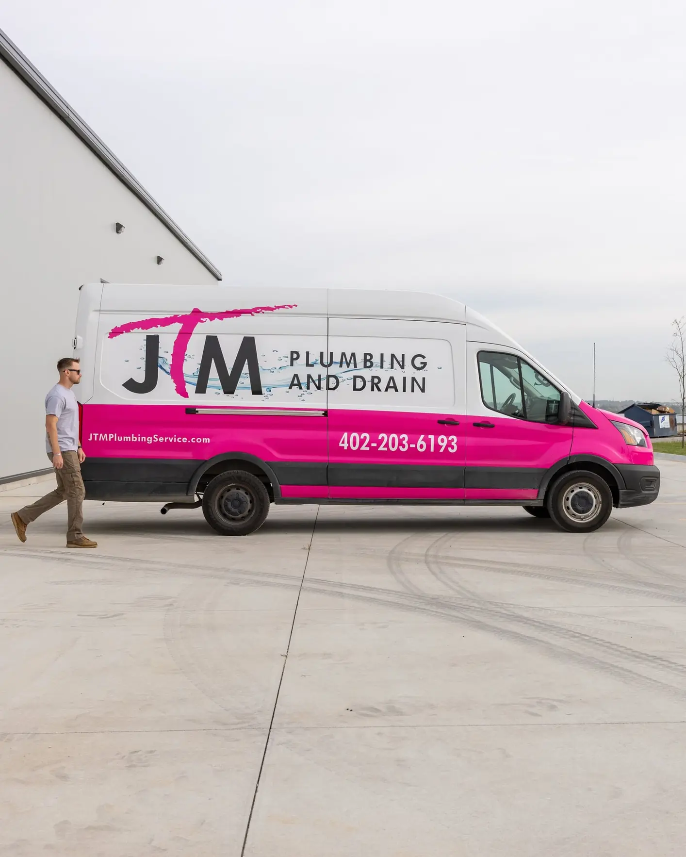 JTM Plumbing & Drain technician walking beside the company van outside a light industrial building.