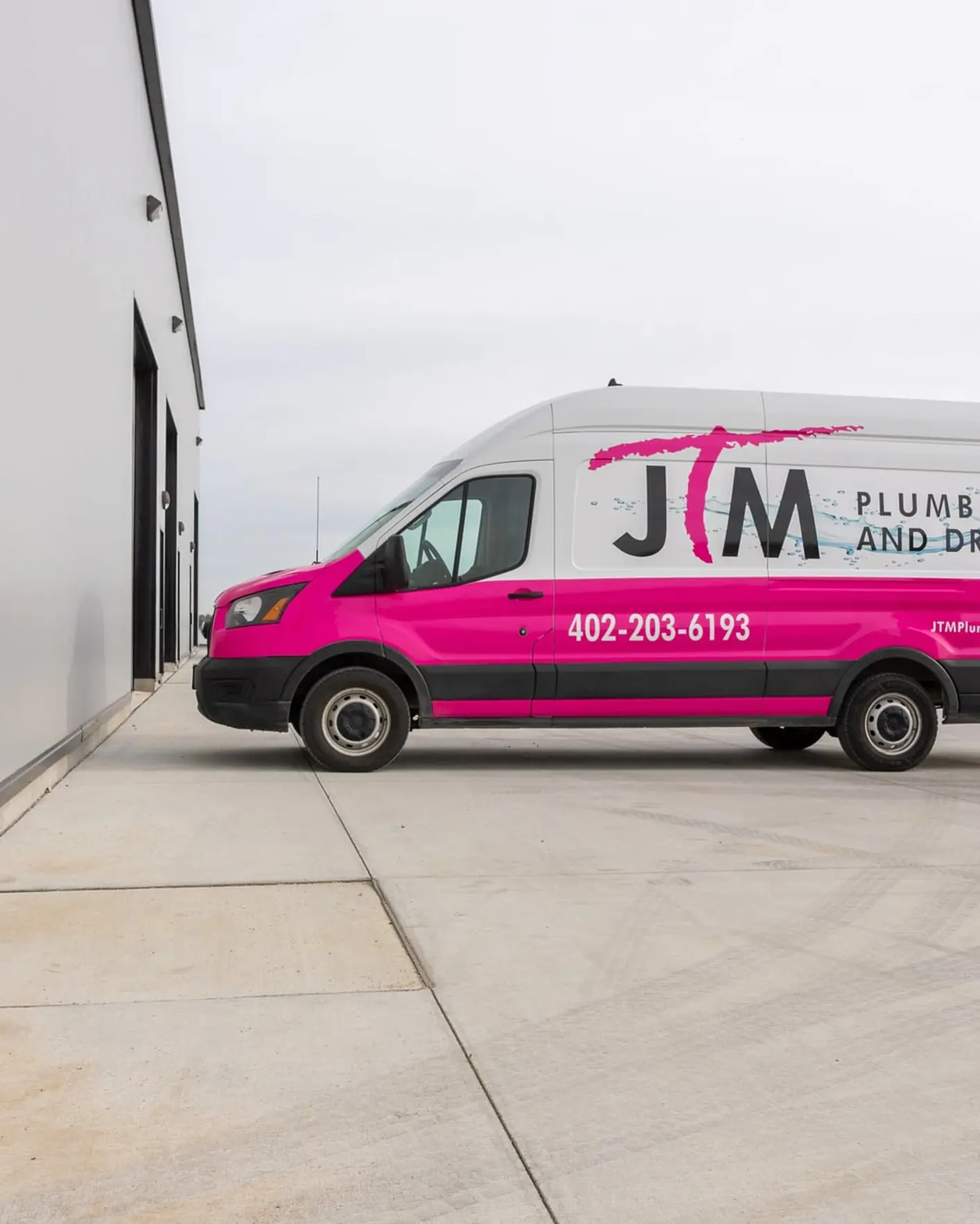 Two JTM Plumbing & Drain technicians walking outside a commercial building beside the branded pink service van.