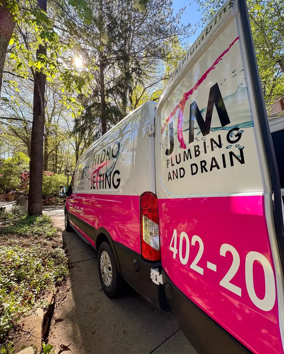 Close-up of the JTM Plumbing & Drain hydro jetting van parked on a tree-lined residential street.