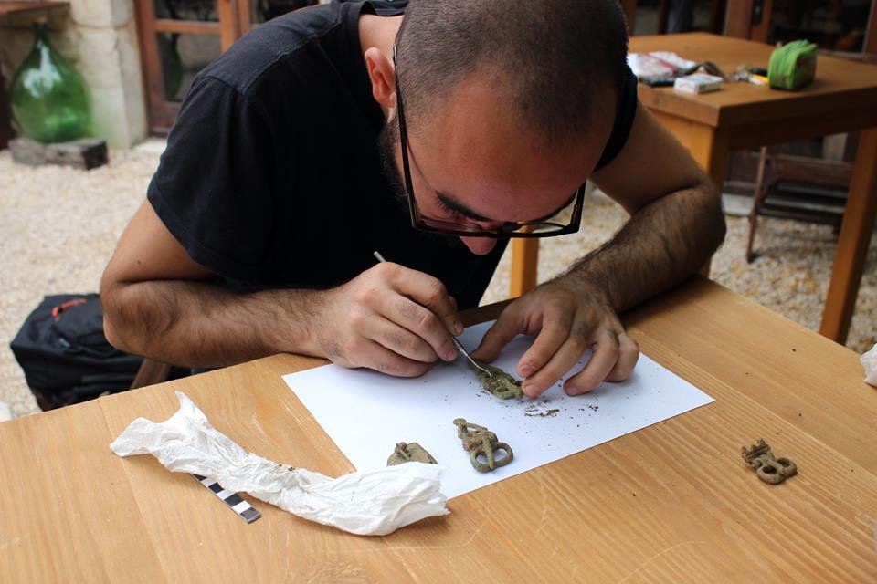 Archaeology student closely examining small medieval artifacts at a table