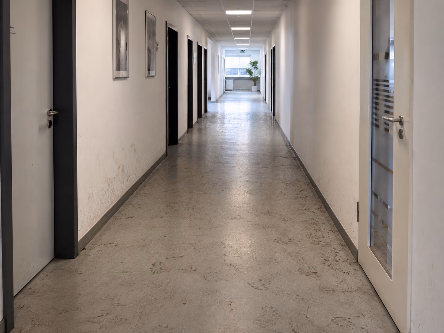Long corridor with multiple closed doors, dirty floors, and scuffed lower walls before cleaning.