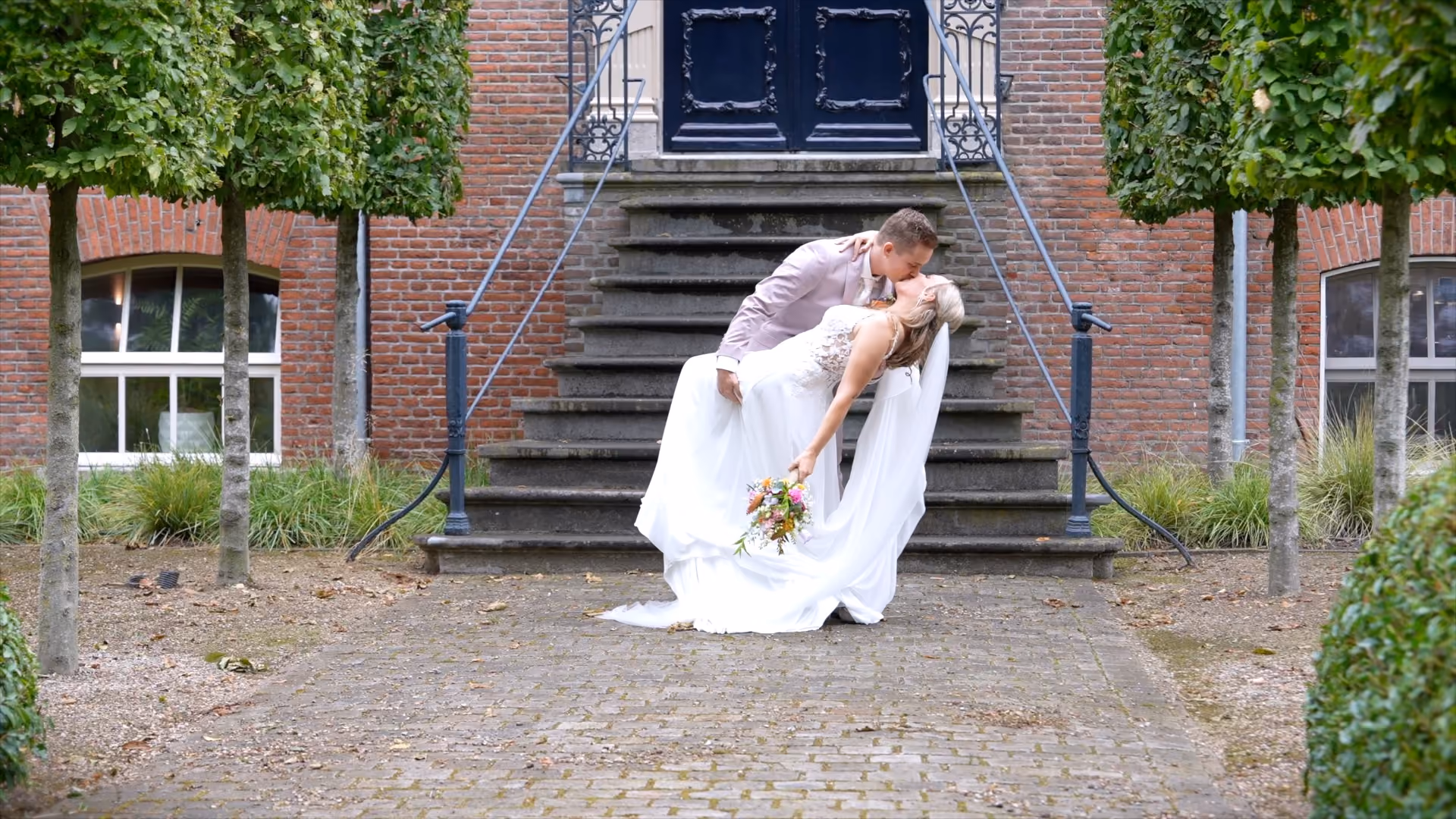 Bruidspaar kust voor de trap van een statig gebouw.
