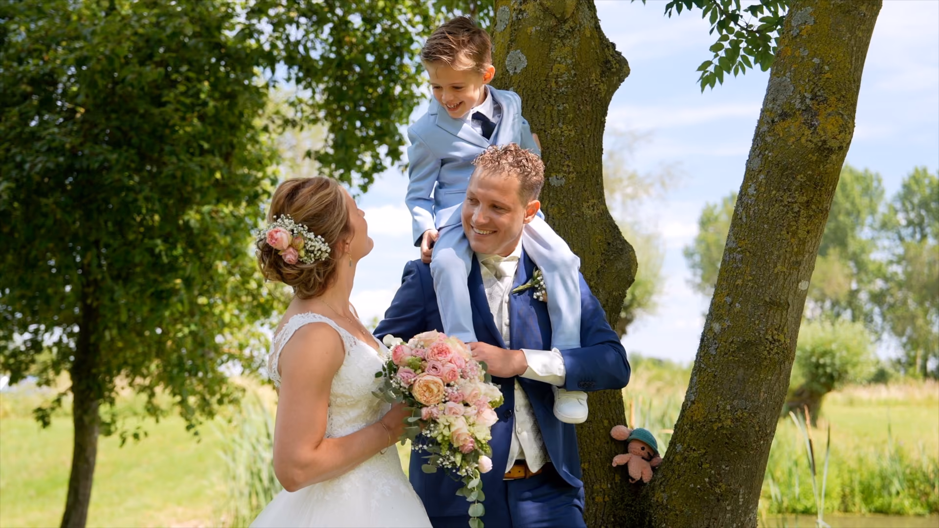 Bruidspaar onder een boom, met een kind op de schouders van de bruidegom.