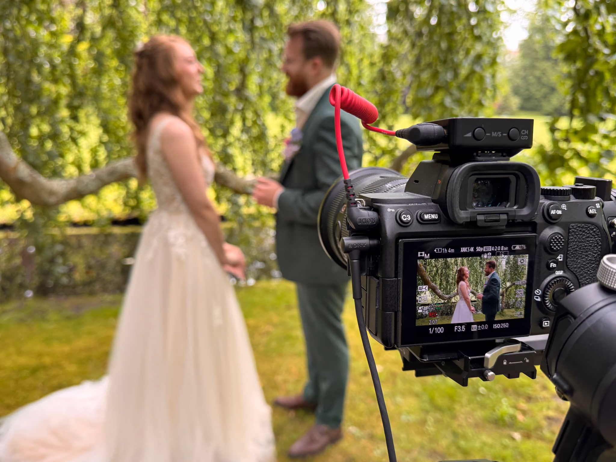 Een camera filmt een bruidspaar onder een boom.
