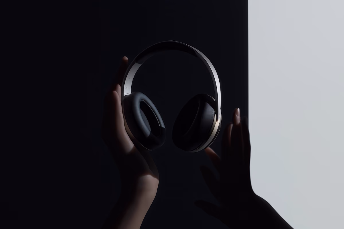 Two hands holding black and silver over-ear headphones against a black and light gray background.