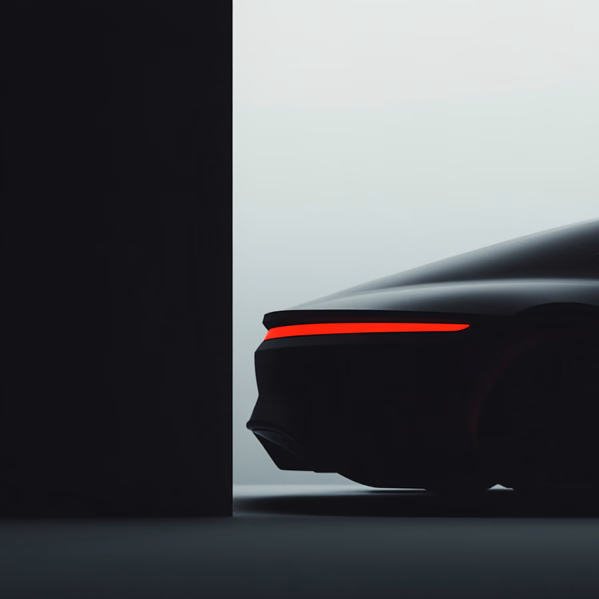 Rear end of a sleek modern black car with illuminated red taillight against gray background.