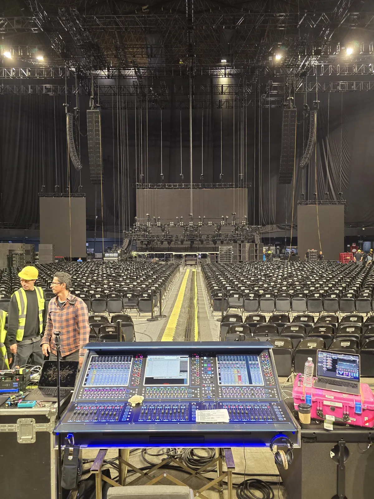 FOH console on its flight case, crew working in an empty arena