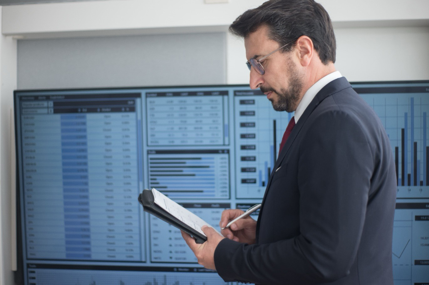 A senior technology leader taking notes in front of a data analytics screen evaluated by technology executive search firms.