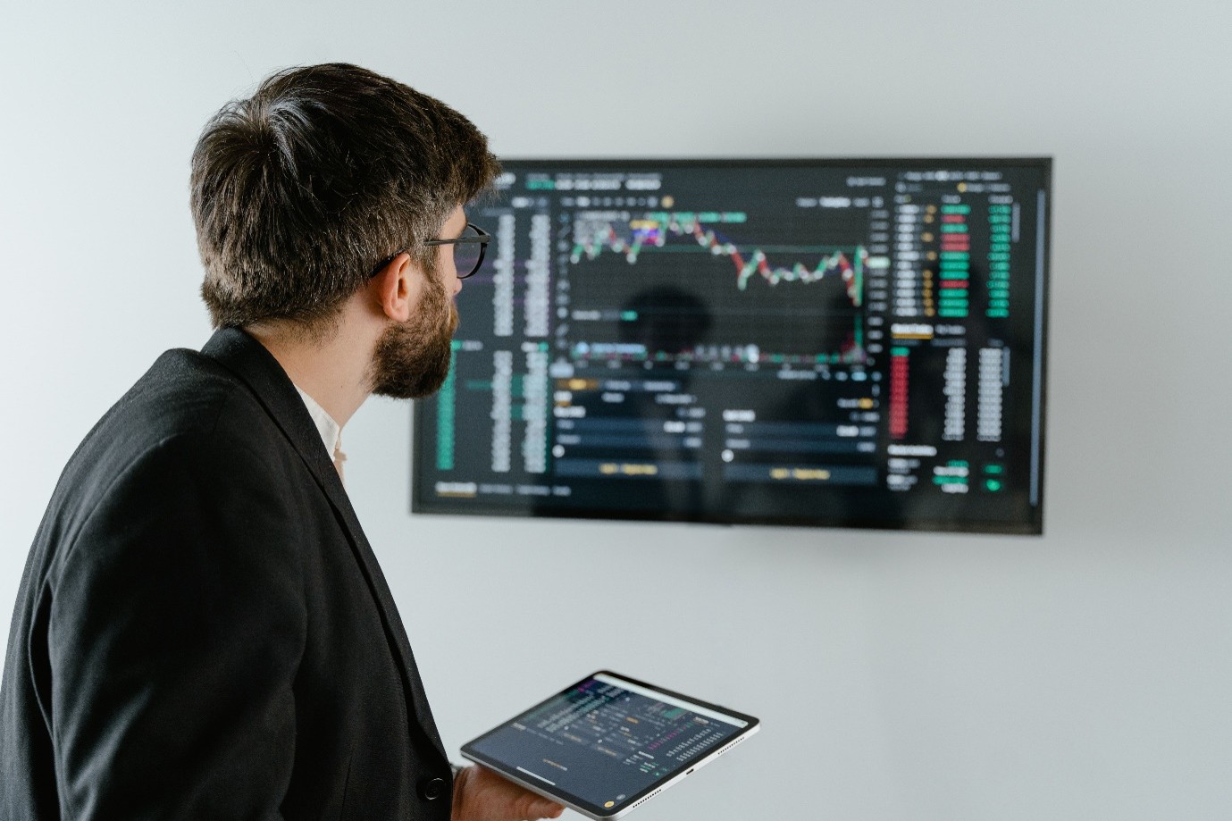 A public sector data analyst reviewing AI in healthcare performance metrics and real-time cloud infrastructure on a large display screen and tablet.