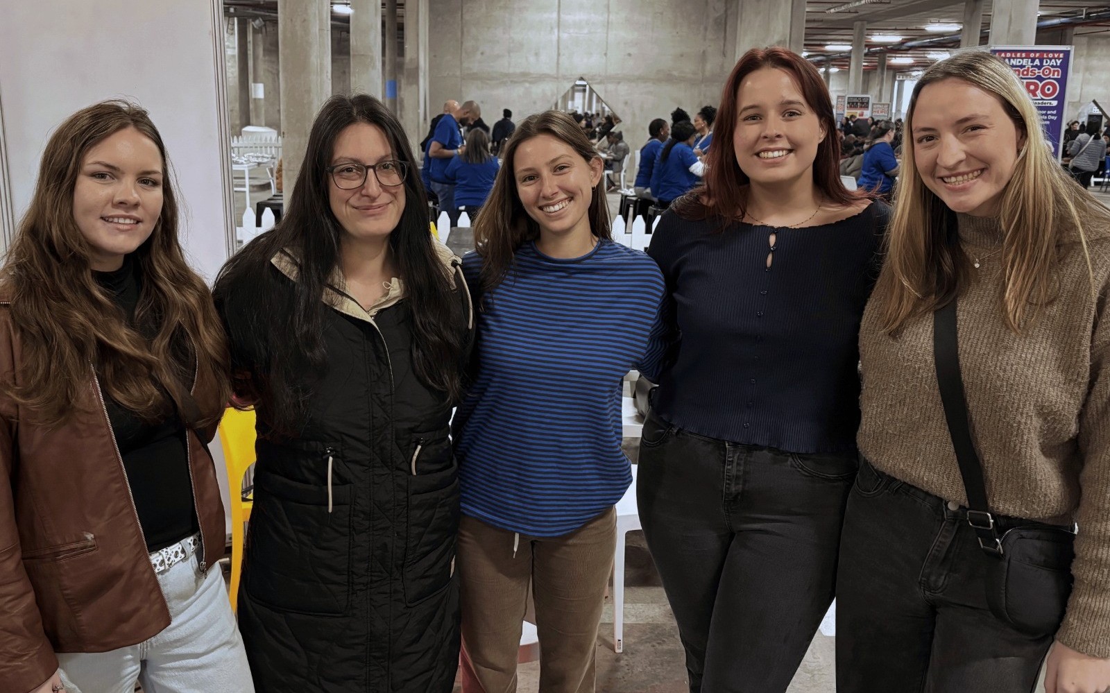 Satigo employees attending a social value event, standing together in an industrial-style venue with attendees and activity visible in the background.