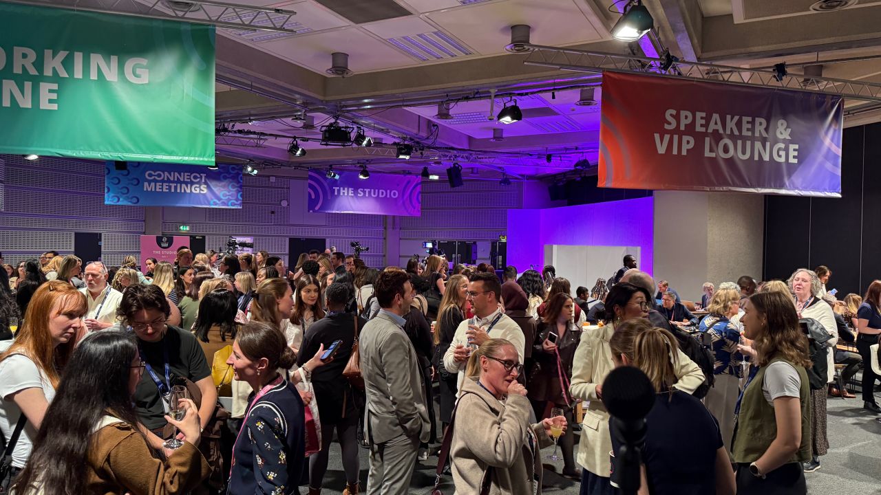 Attendees networking and engaging in conversations at a busy conference event, with meeting spaces and a VIP lounge visible in the venue.
