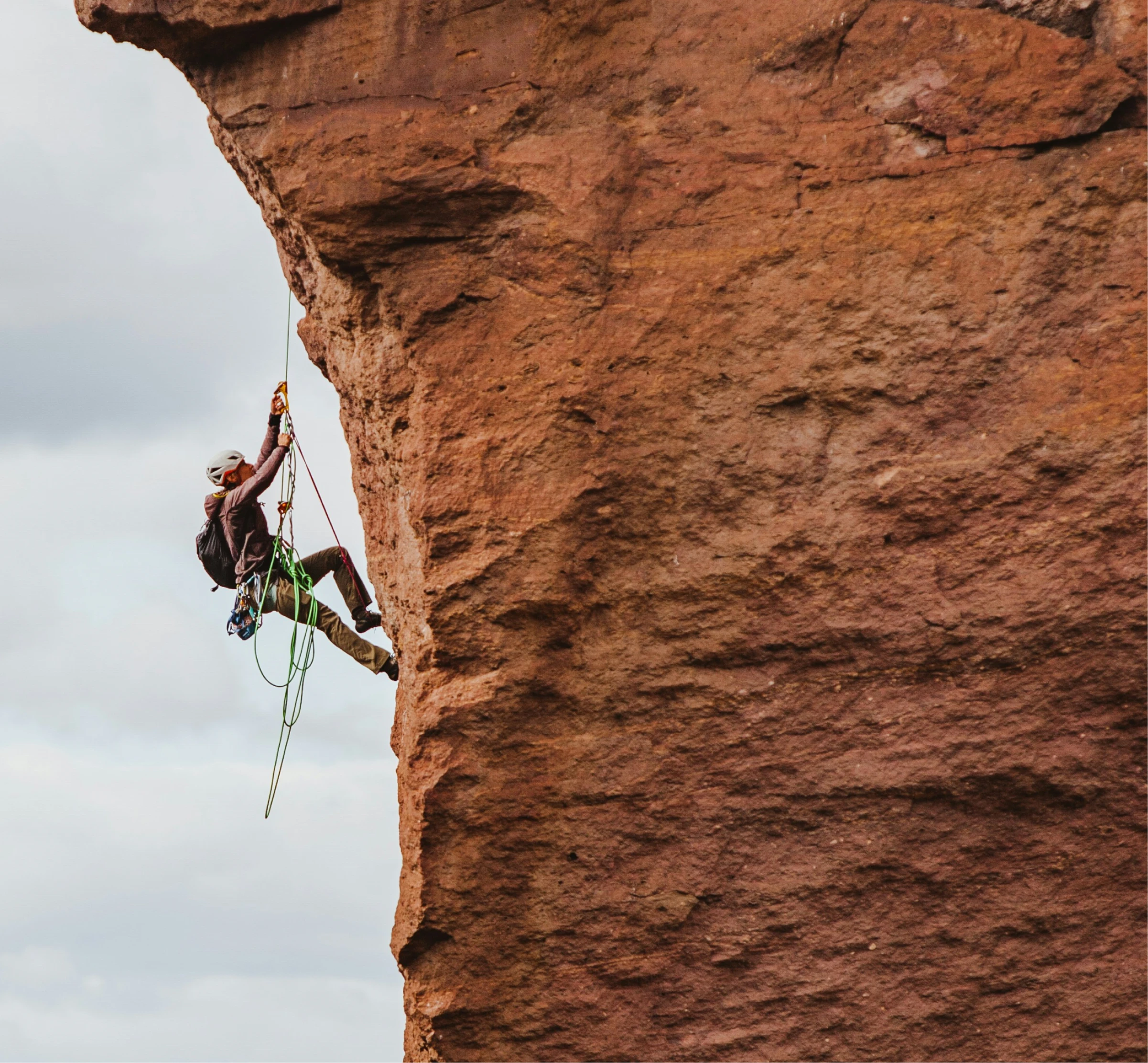 Un grimpeur portant un casque descend une falaise rocheuse rouge avec des cordes.