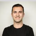 Homme souriant aux cheveux courts et portant un t-shirt noir sur fond clair.