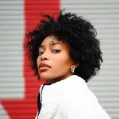 Portrait d'une femme avec un pull blanc et cheveux afro, arrière-plan rouge et blanc flou.