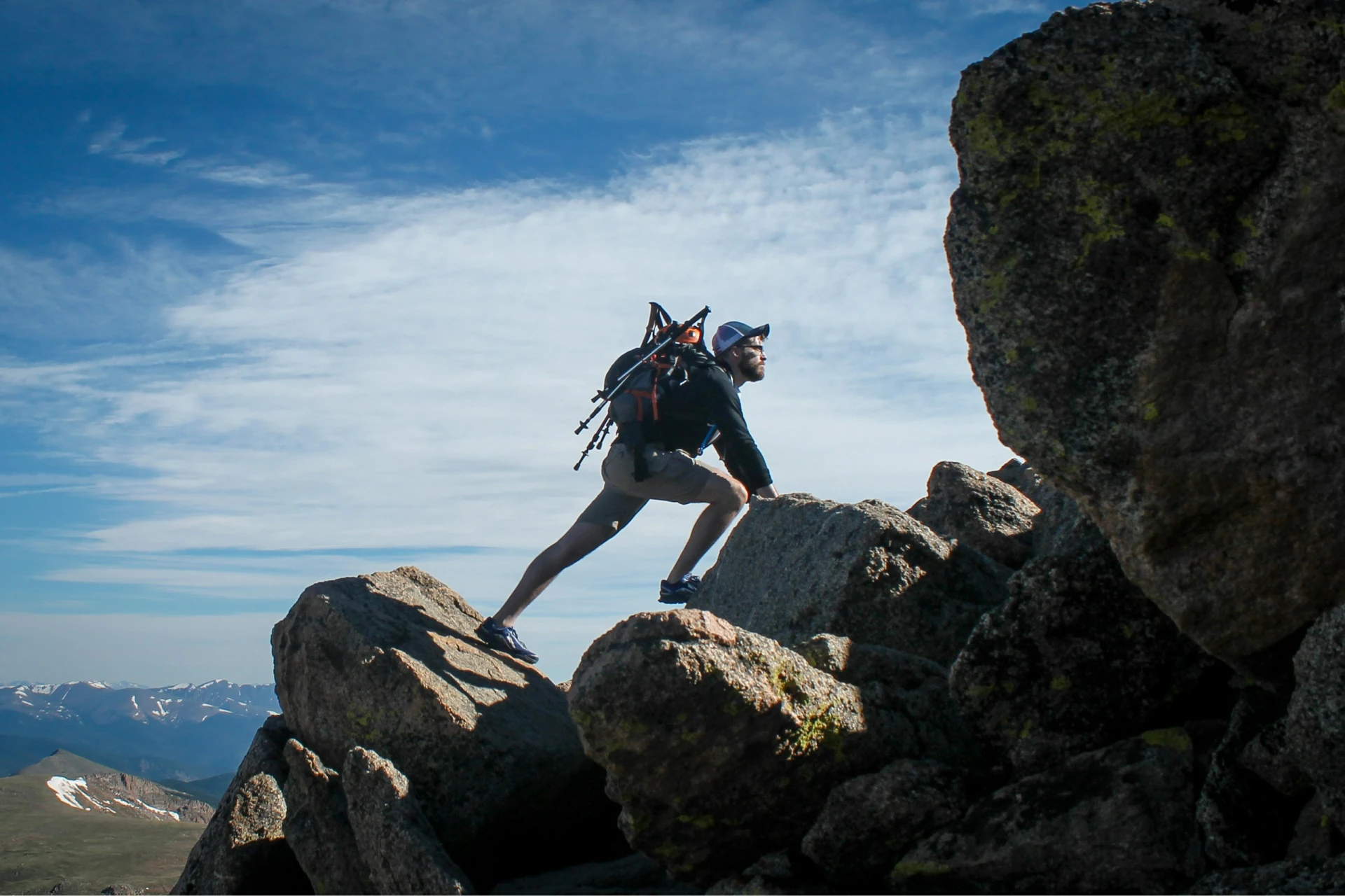 Un homme avec un sac à dos escalade des rochers sous un ciel bleu avec des nuages.