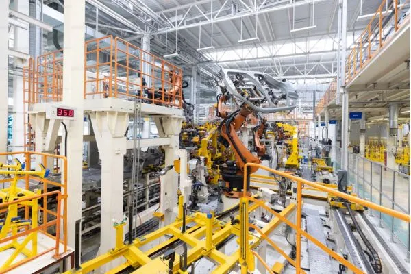 Vue d'une usine automatisée avec des robots industriels et des structures métalliques jaunes et blanches.