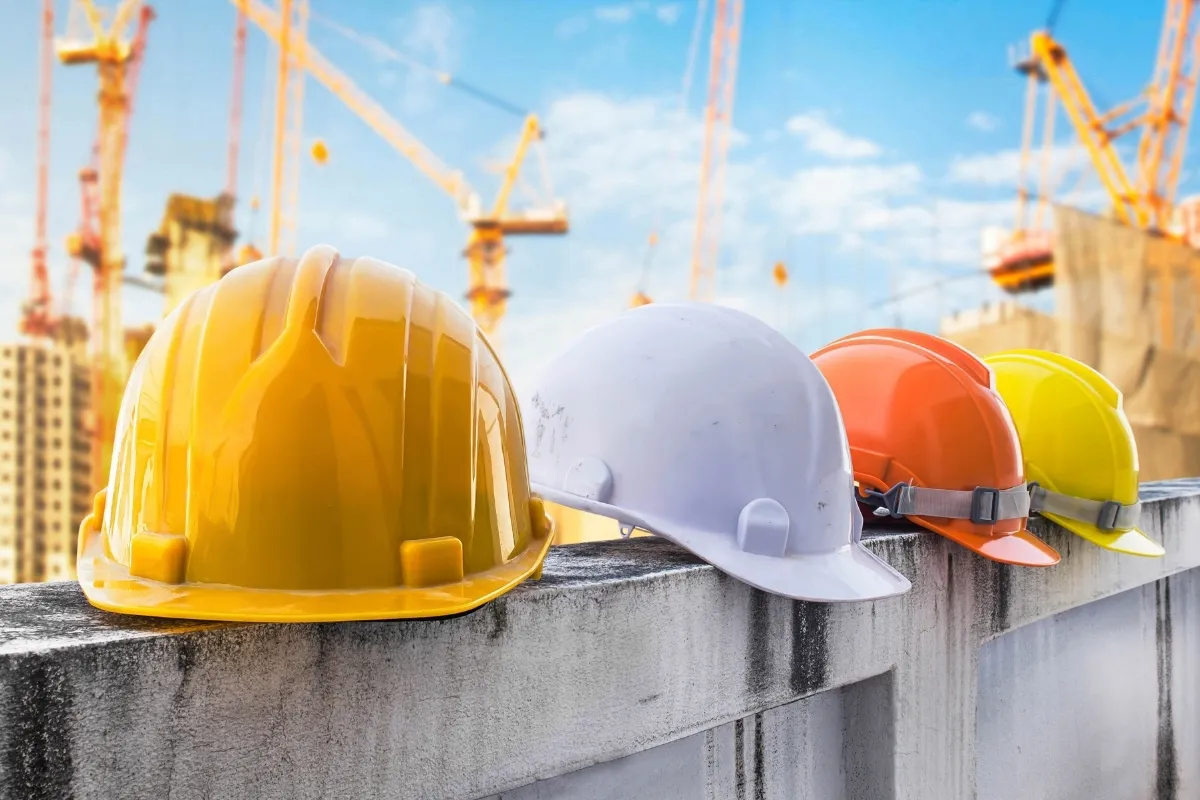 Casques de sécurité de couleurs jaune, blanc, orange et jaune posés sur un mur au chantier.