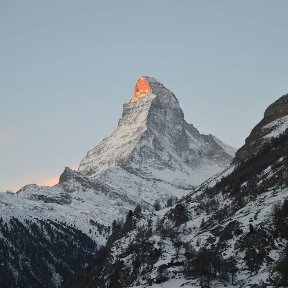 Sommet de montagne enneigé avec la lumière du soleil couchant illuminant son pic.