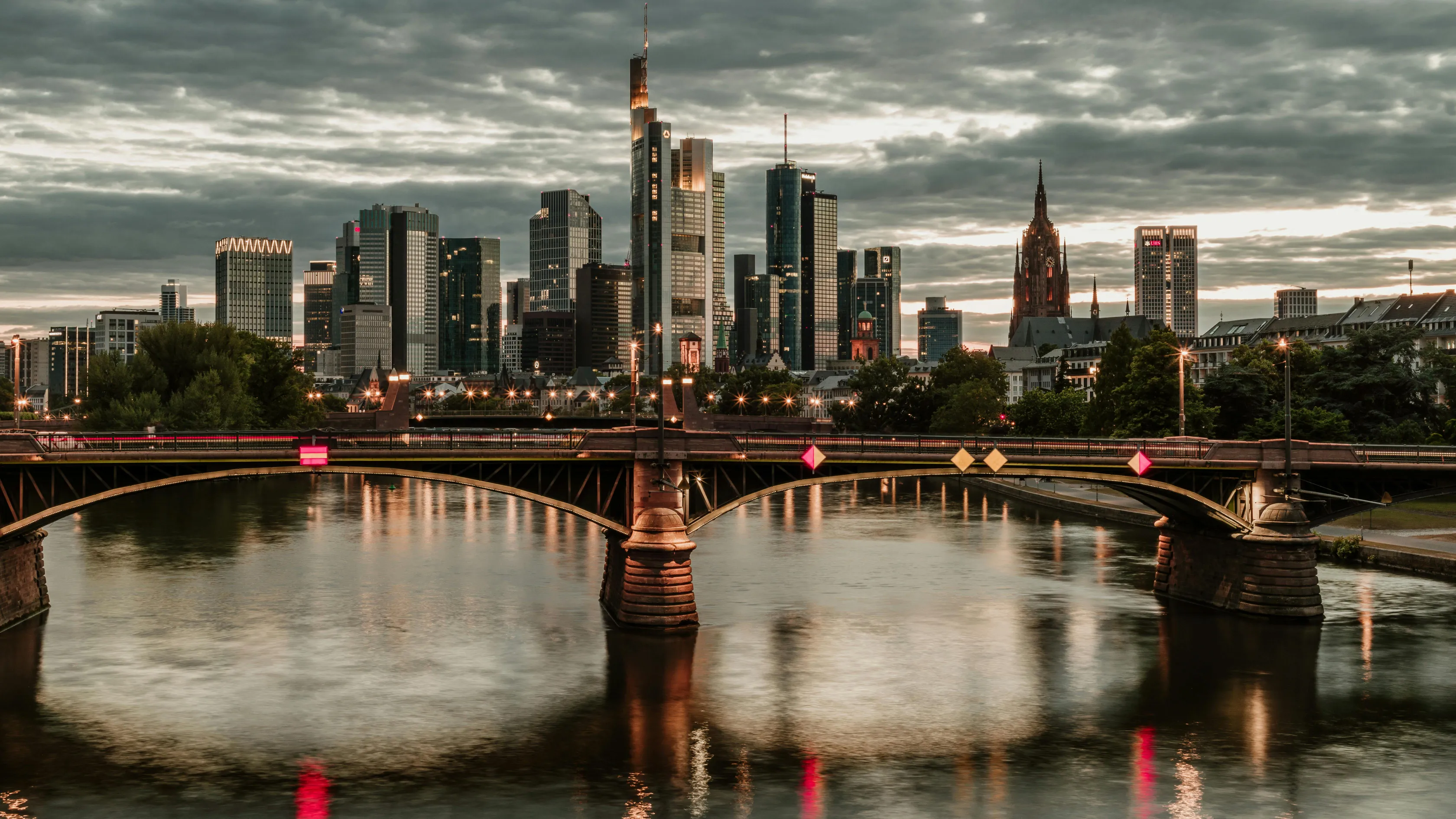 Escort Frankfurt - Skyline von Frankfurt am Main bei Sonnenuntergang mit beleuchteter Brücke über den Main.