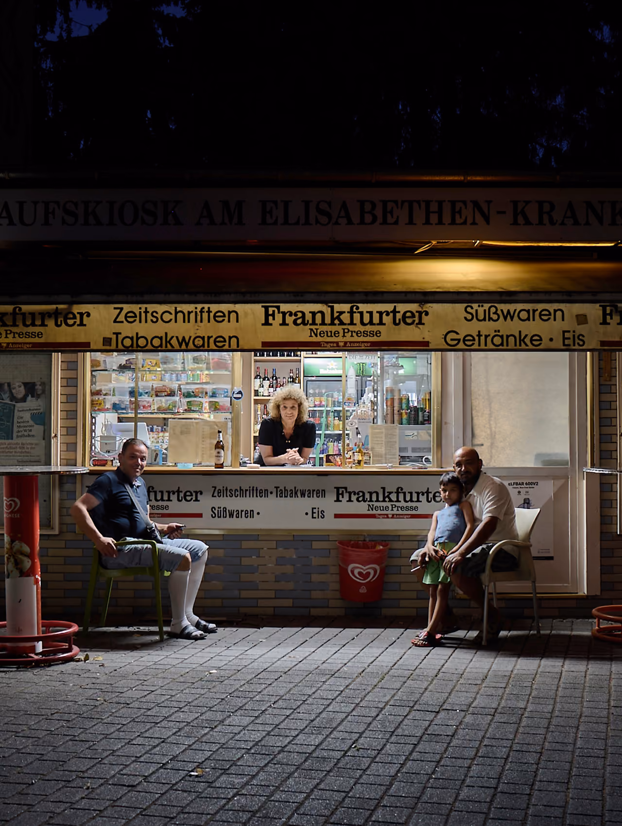 Verkaufskiosk bei Nacht, Gäste sitzen auf Stühlen davor
