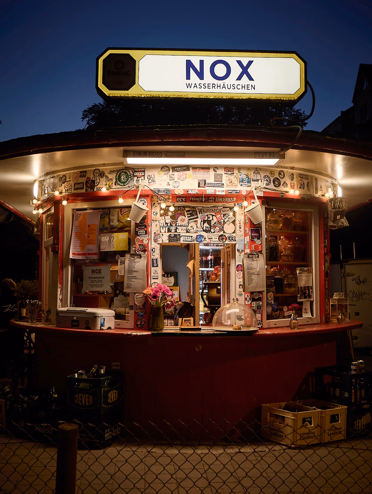 Wasserhäuschen NOX in der Dämmerung mit beleuchtetem Schild und Verkaufsfenster