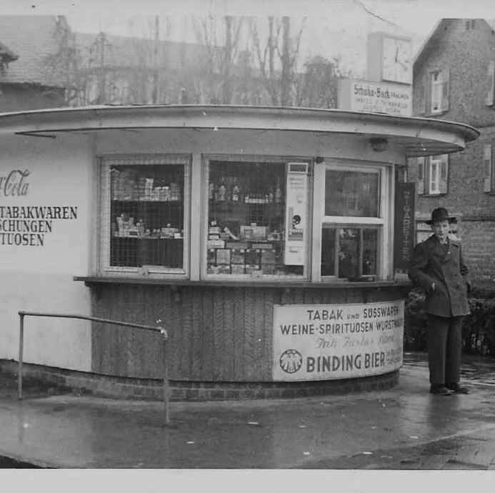 Historisches Wasserhäuschen mit Werbung für Tabak, Süßwaren und Binding Bier, daneben ein Mann mit Hut