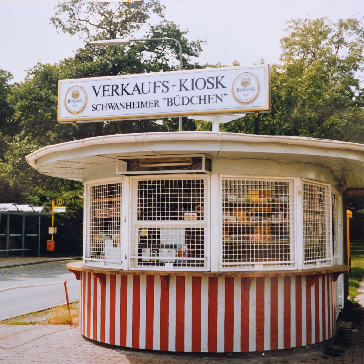 Runder Verkaufskiosk mit der Aufschrift Schwanheimer Büdchen und rot-weiß gestreiftem Sockel