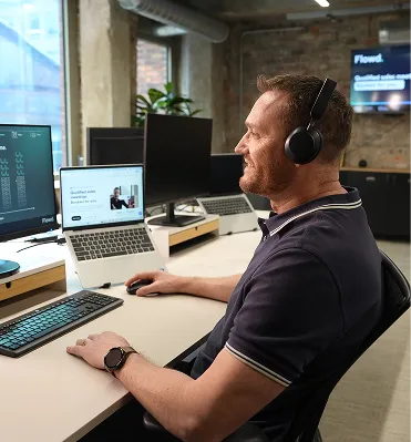 Man wearing headphones and using a laptop at a desk in a modern office setting.