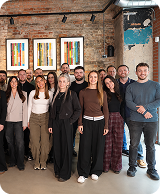 Group of diverse young adults standing indoors in front of a brick wall with colorful artwork.