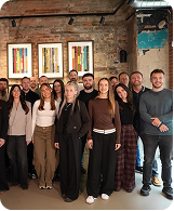 Group of diverse young adults standing indoors in front of a brick wall with colorful artwork.