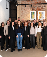 Group portrait of men and women standing in an indoor room with brick walls and framed art.