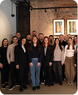 Group portrait of men and women standing in an indoor room with brick walls and framed art.
