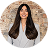 Smiling woman with long dark hair wearing a light gray blazer against a brick wall.