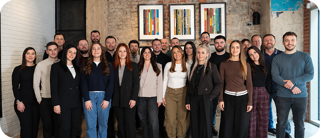 Group photo of 22 men and women standing in an indoor space with brick and white walls.