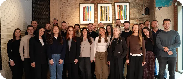 Group photo of 22 men and women standing in an indoor space with brick and white walls.