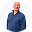 Smiling older man with white beard and blue shirt waving with one hand in front of a white background.