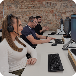 Three people wearing headsets working on computers in an office with a brick wall background.