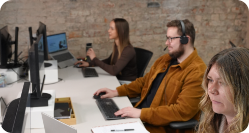 Man with headset and woman working on laptops in modern office with exposed brick wall.