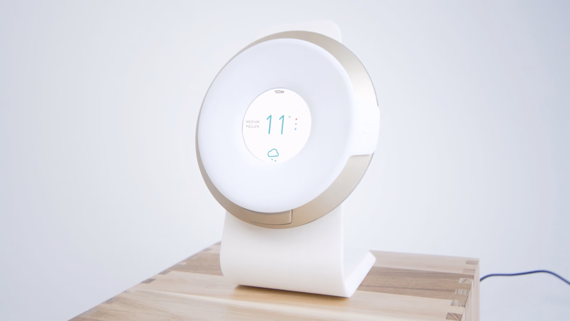 Round digital weather monitor displaying temperature 11° and medium pollen level on a wooden table.