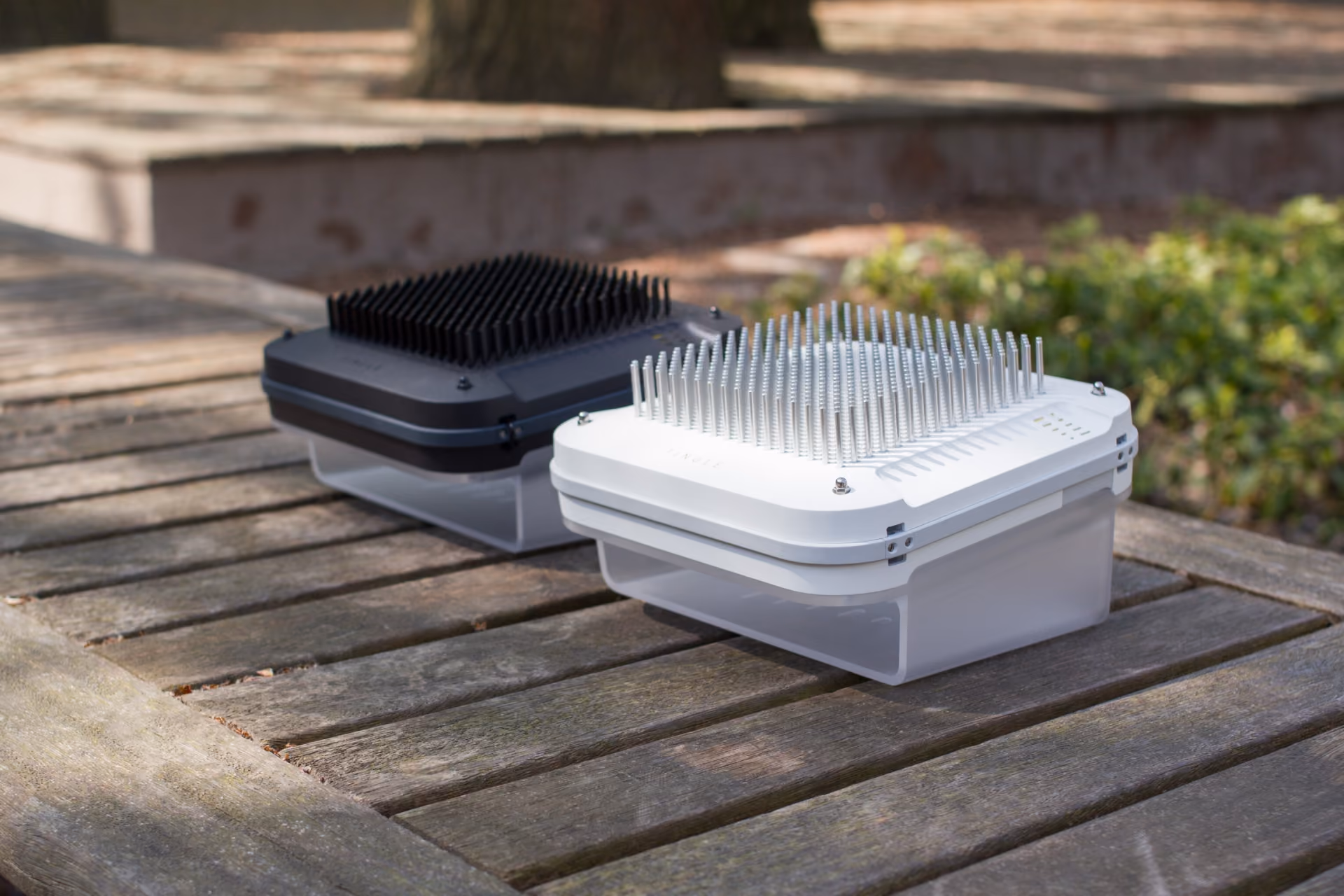 Two rectangular electronic devices with metal pin arrays on top placed on a wooden outdoor table.
