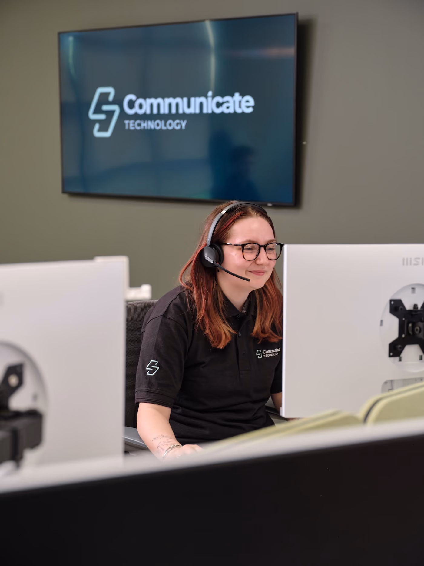 Woman wearing headset and glasses working at a computer with Communicate Technology logo on screen.
