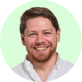 Smiling man with short brown hair and beard wearing a white buttoned shirt on light green background.
